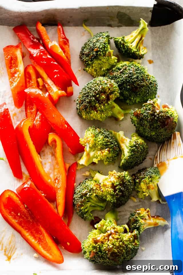 Red bell pepper slices and broccoli florets arranged on a baking sheet, ready for roasting.