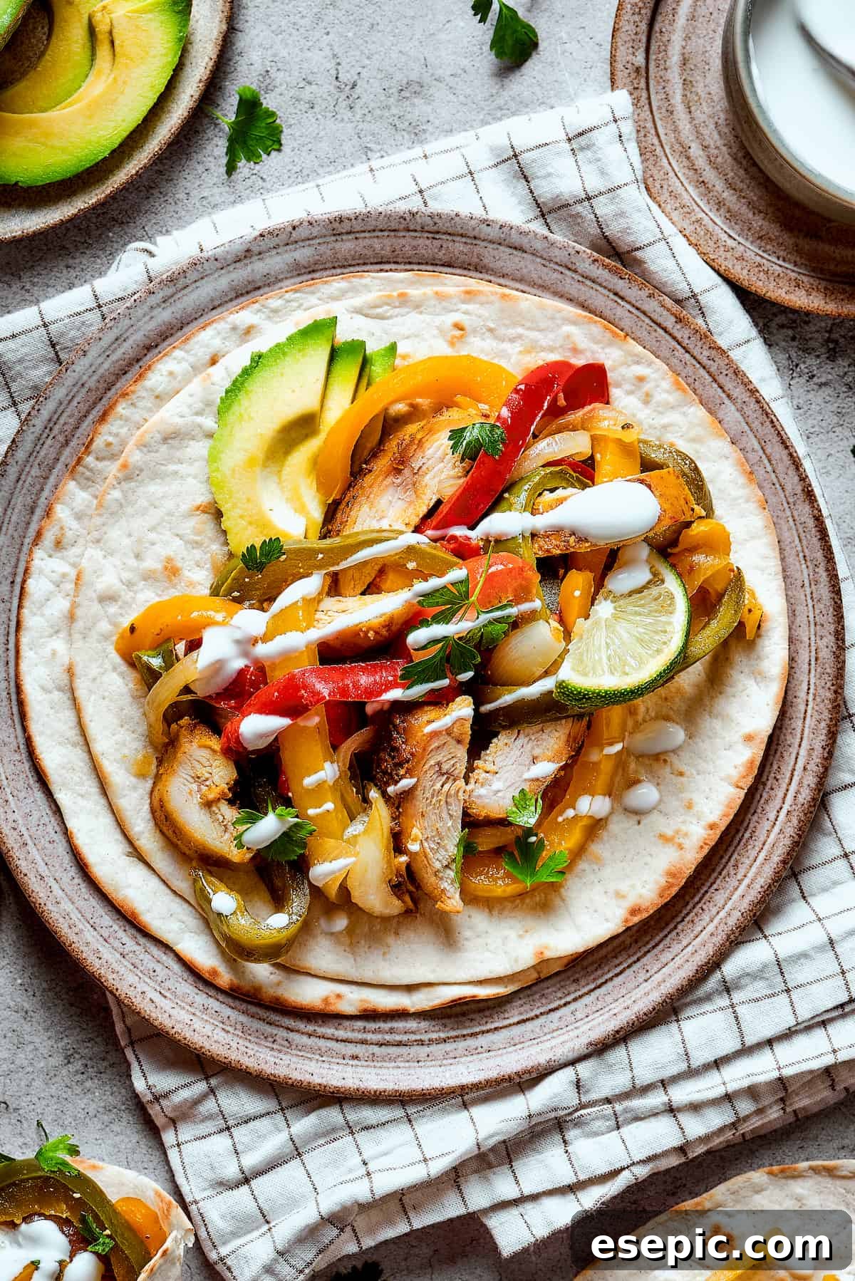 Crockpot chicken fajitas plated ad topped with lime, avocado, and sour cream.