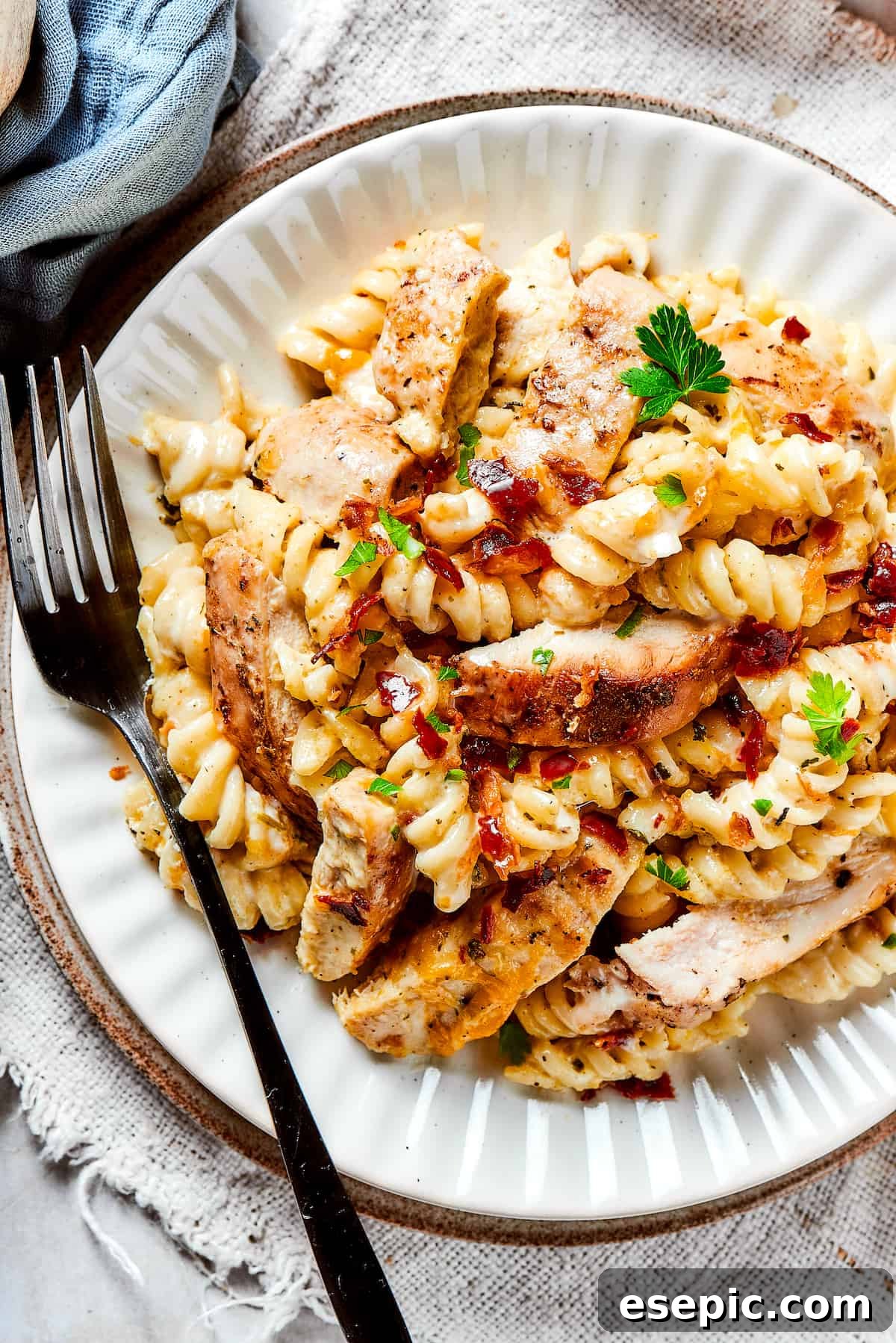 A dinner plate featuring a generous serving of creamy Chicken Bacon Ranch Pasta, garnished with fresh parsley and extra bacon crumbles.