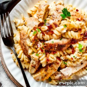 A dinner plate of pasta and chicken with creamy sauce and bacon.