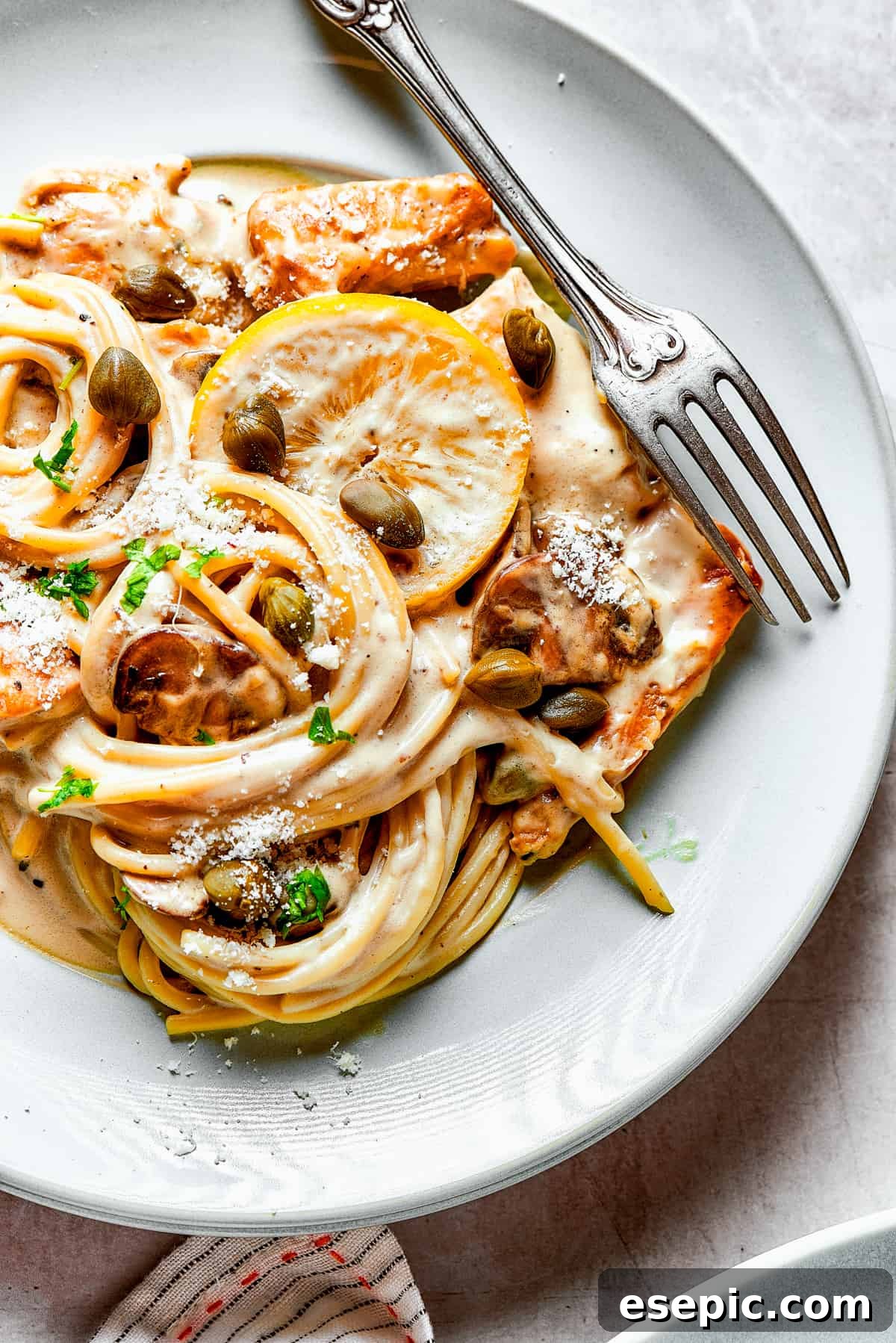 An overhead view of a generous serving of chicken piccata pasta on a dinner plate, accompanied by a fork, inviting you to dig in.