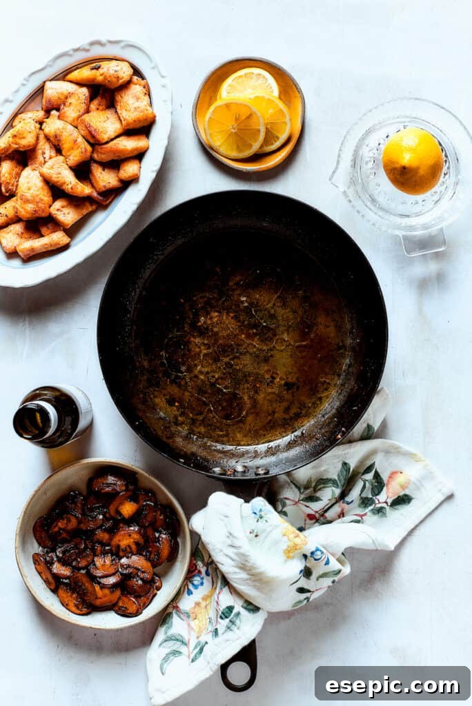 Cooked mushrooms and chicken strips resting on a plate beside a simmering skillet, awaiting their return to the sauce.