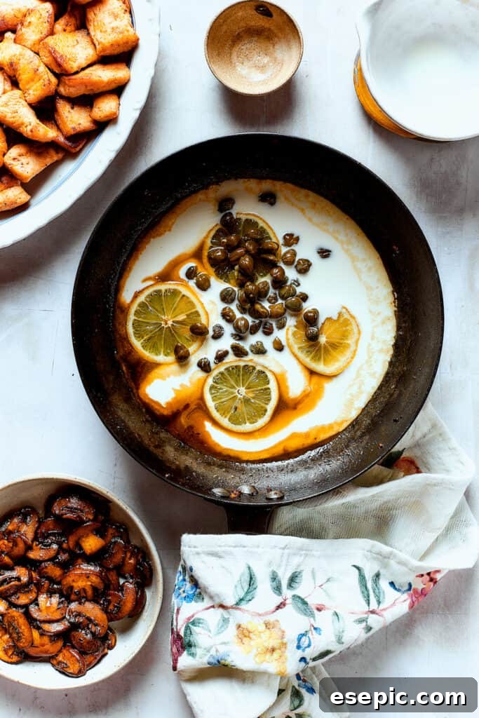 A creamy caper and lemon sauce simmering in a skillet, building depth of flavor before the final ingredients are added.