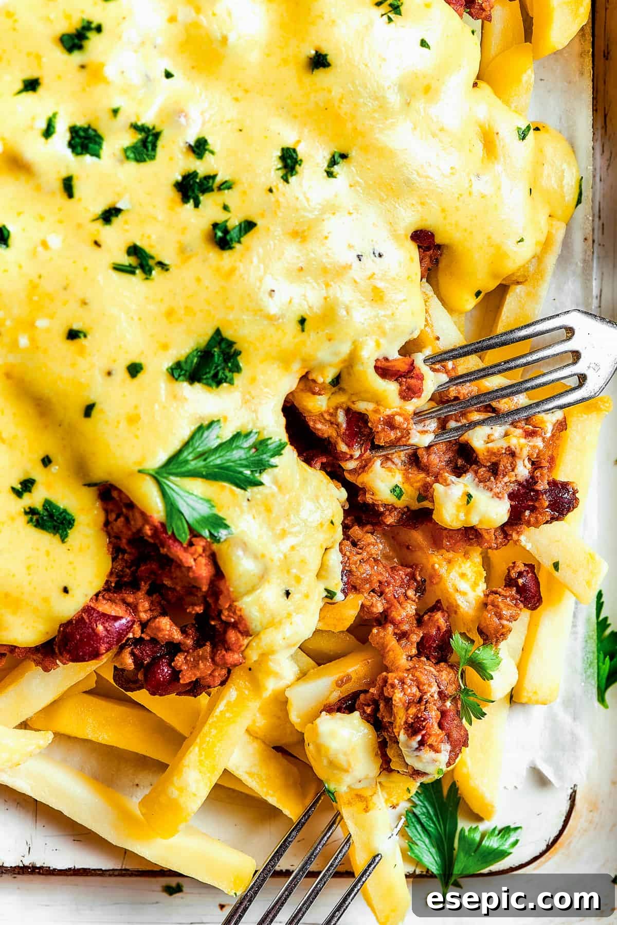 You’ll crave the hot, cheesy goodness of homemade Chili Cheese Fries! This is a fun party appetizer that can double as a family-style meal. A fork taking a bite from a batch of chili cheese fries.
