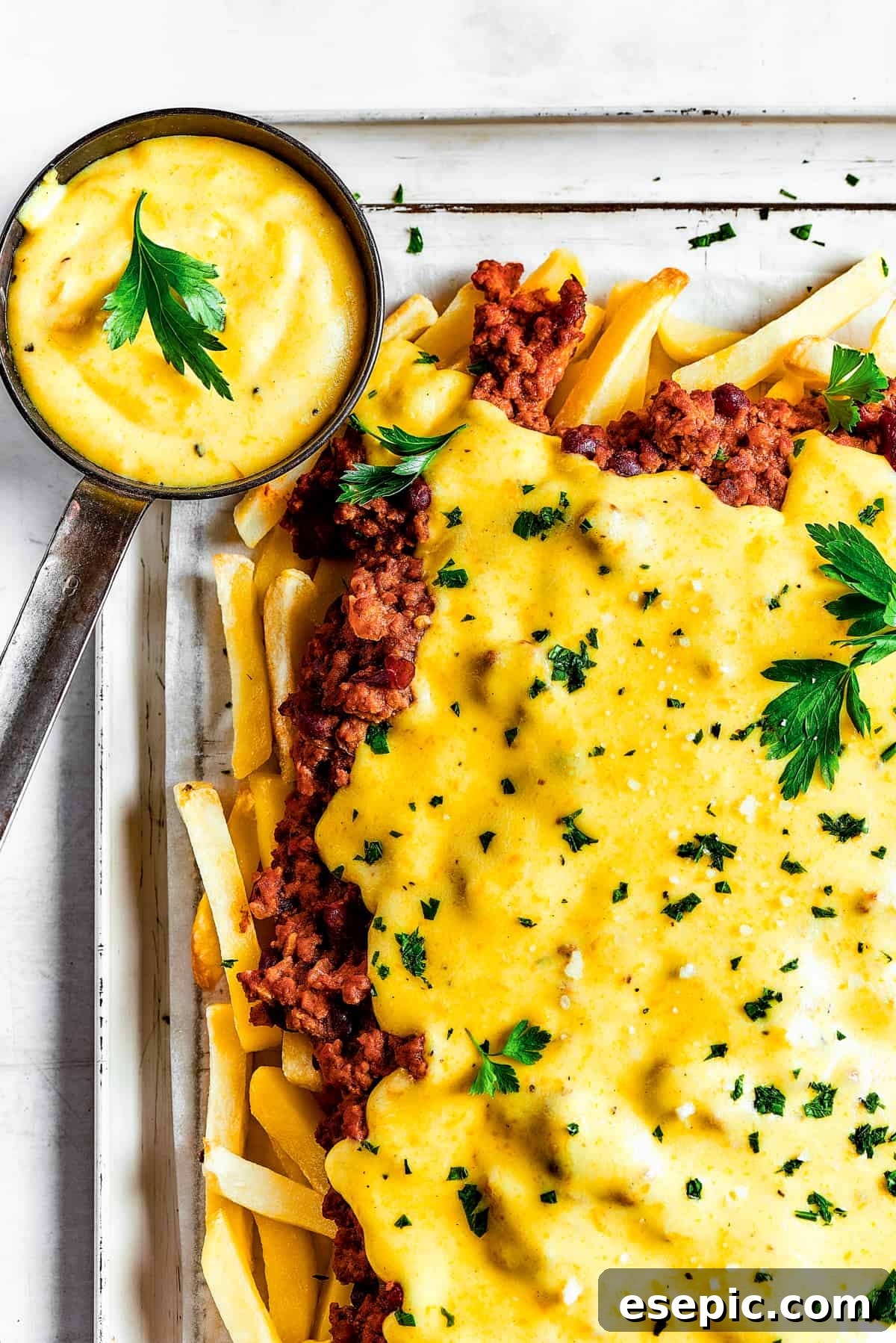 You’ll crave the hot, cheesy goodness of homemade Chili Cheese Fries! This is a fun party appetizer that can double as a family-style meal. Homemade chili cheese fries with dipping sauce and a blue tea towel.