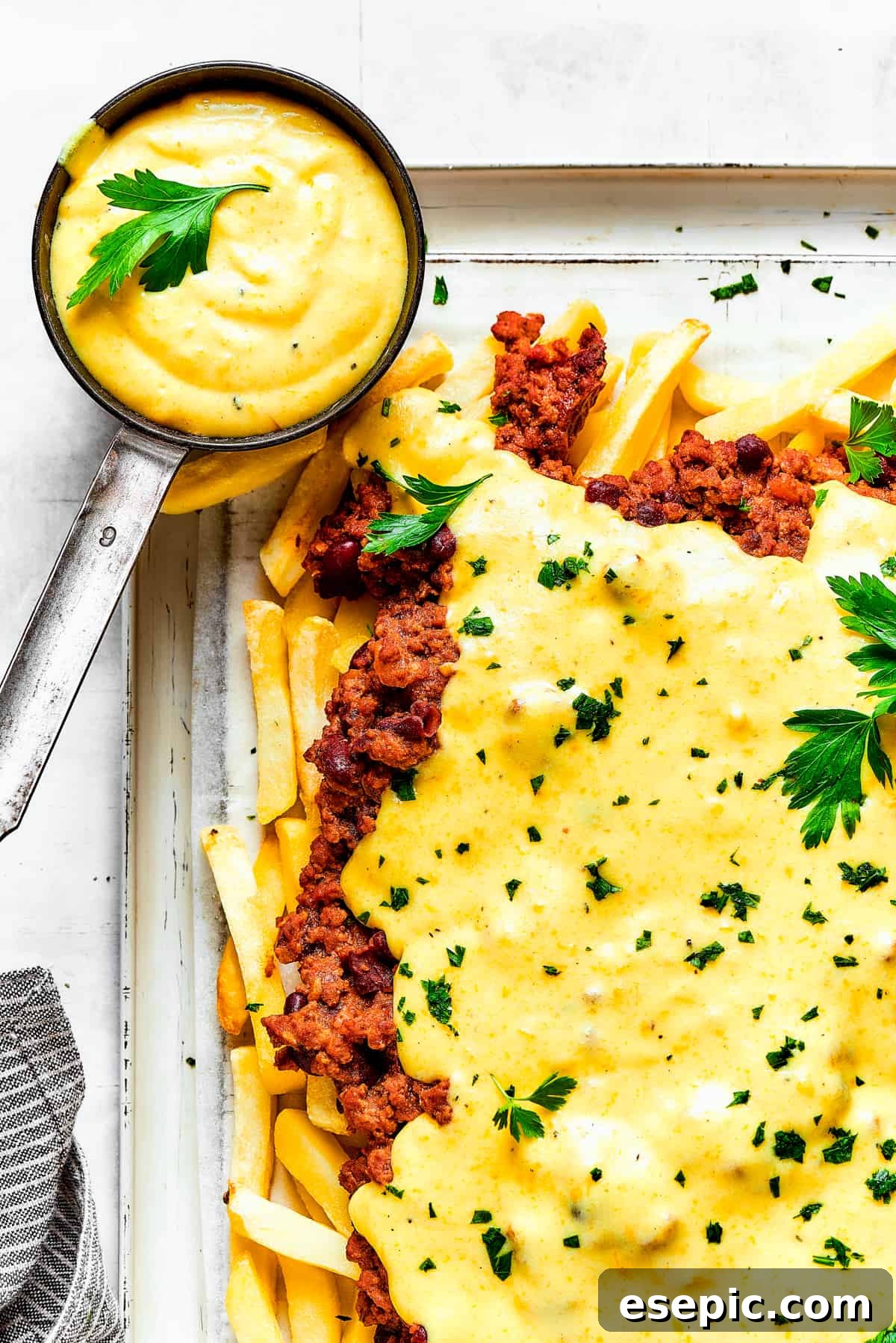 You’ll crave the hot, cheesy goodness of homemade Chili Cheese Fries! This is a fun party appetizer that can double as a family-style meal. Homemade chili cheese fries with dipping sauce and a blue tea towel.