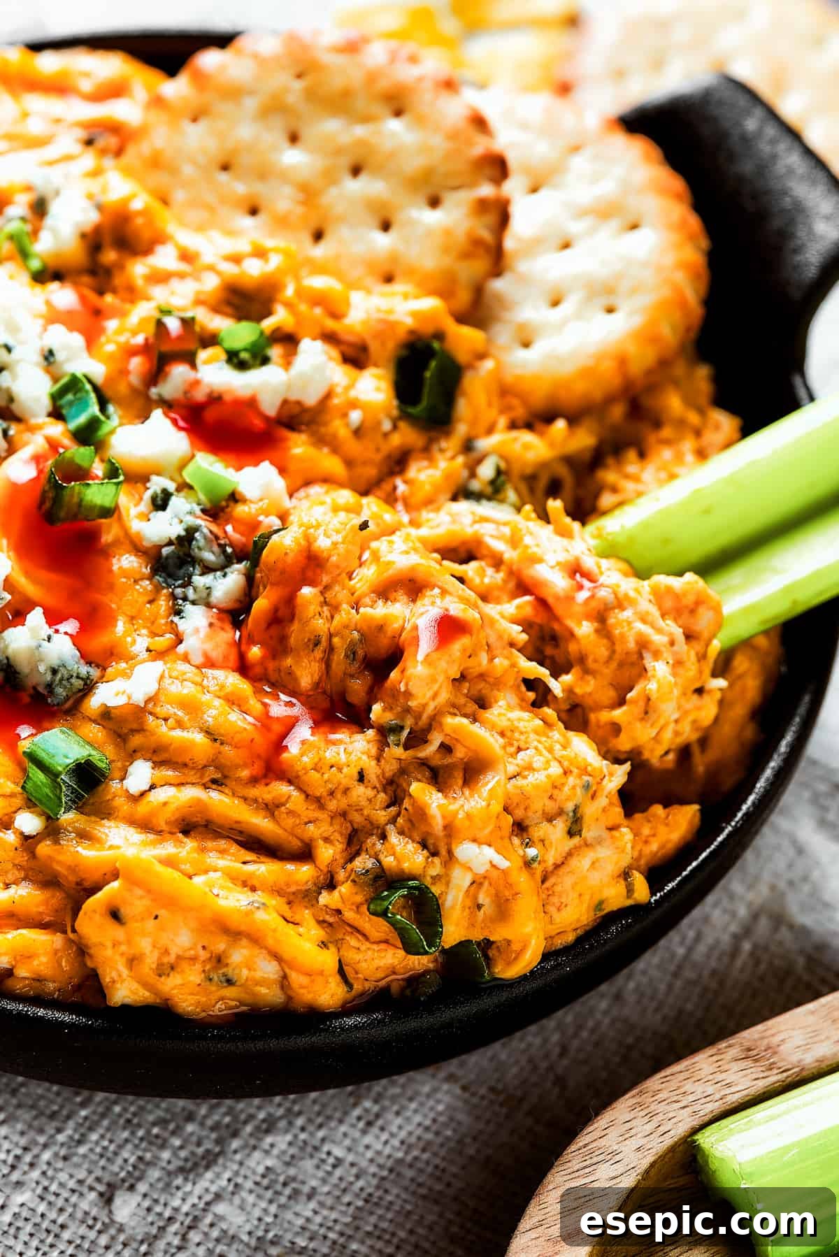 With its creamy, cheesy, spicy goodness, Crockpot Buffalo Chicken Dip is a favorite for parties, game days, movie nights, and more. A small, elegant two-handled dish brimmed with steaming Crockpot Buffalo Chicken Dip, artfully garnished with vibrant green onions, surrounded by crisp celery sticks and an assortment of golden crackers, ready for communal enjoyment.