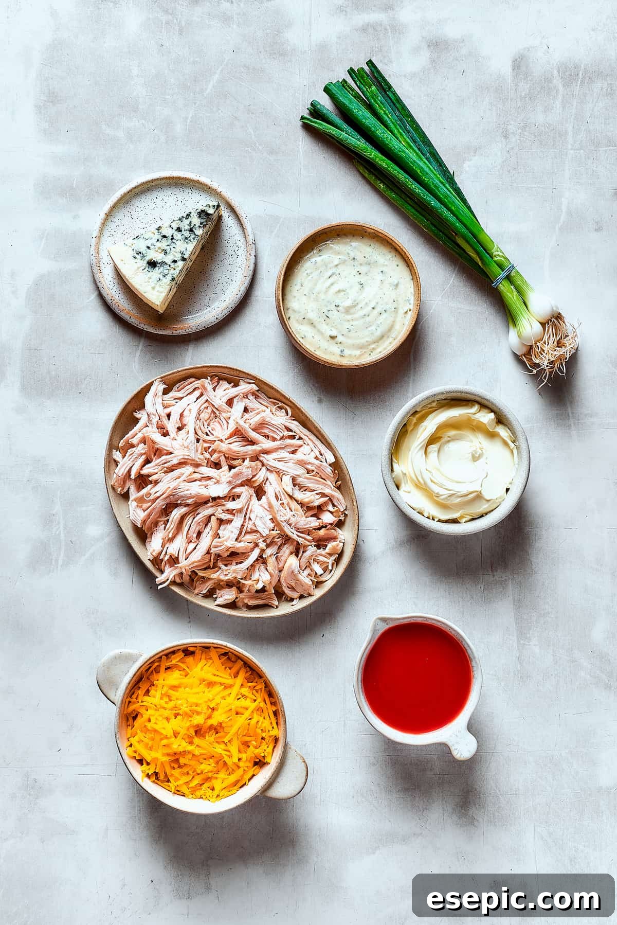 With its creamy, cheesy, spicy goodness, Crockpot Buffalo Chicken Dip is a favorite for parties, game days, movie night, and more! A vibrant flat lay of all the essential ingredients for Crockpot Buffalo Chicken Dip, neatly arranged on a rustic wooden table: shredded chicken, various cheeses, hot sauce, ranch dressing, and fresh green onions, showcasing their readiness for preparation.
