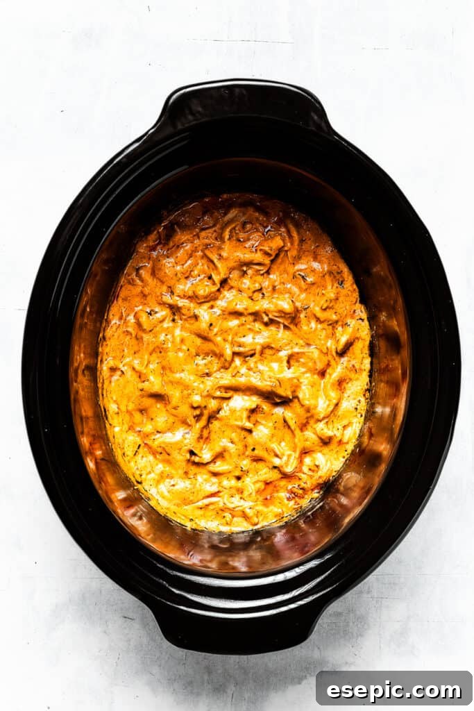 With its creamy, cheesy, spicy goodness, Crockpot Buffalo Chicken Dip is a favorite for parties, game days, movie night, and more! A vibrant close-up shot of a slow cooker filled with bubbling, perfectly cooked Crockpot Buffalo Chicken Dip, its cheesy, creamy texture ready to be scooped and enjoyed, with wisps of steam rising, indicating its warmth and freshness.