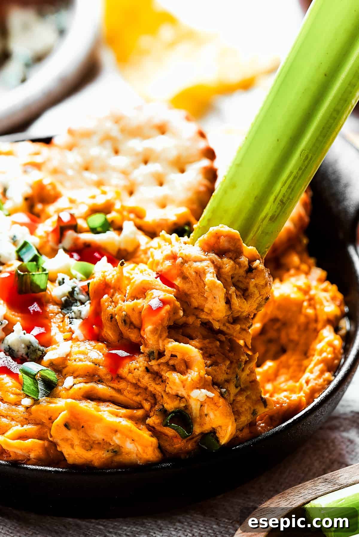 With its creamy, cheesy, spicy goodness, Crockpot Buffalo Chicken Dip is a favorite for parties, game days, movie night, and more! A close-up shot of creamy Crockpot Buffalo Chicken Dip generously garnished with vivid green onions and savory blue cheese crumbles, with a fresh celery stick artfully dipped in, ready to be enjoyed as a perfect snack.