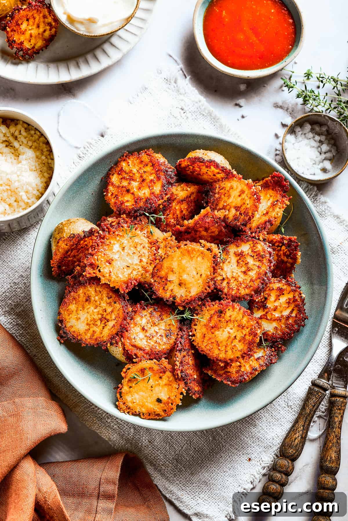 A bowl of baked potato halves crusted with parmesan cheese, garnished with fresh herbs.