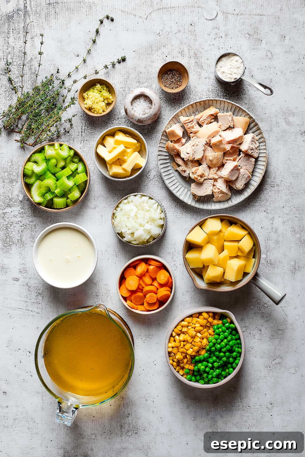 Hearty and comforting chicken pot pie soup has a rich and creamy broth, tender veggies, and juicy chicken, and is so easy to make. Overhead view of the meticulously arranged ingredients needed for chicken pot pie soup. Bowls contain golden chicken broth, rich heavy cream, vibrant peas and corn, diced carrots, cubed potatoes, chopped onions, minced garlic, sliced celery, a stick of butter, cooked chicken pieces, fresh thyme sprigs, salt, pepper, and a measuring cup of flour, all ready for cooking.
