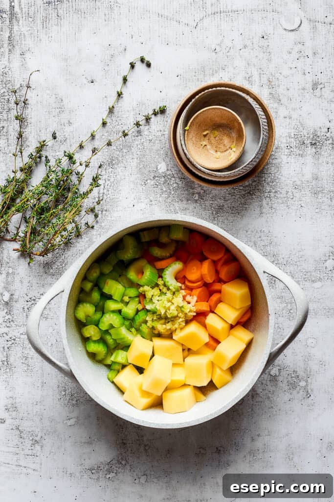 Sautéing fresh vegetables for chicken pot pie soup. A large pot filled with a colorful mix of chopped onions, carrots, celery, and potatoes, ready for sautéing, with fresh thyme sprigs nearby.