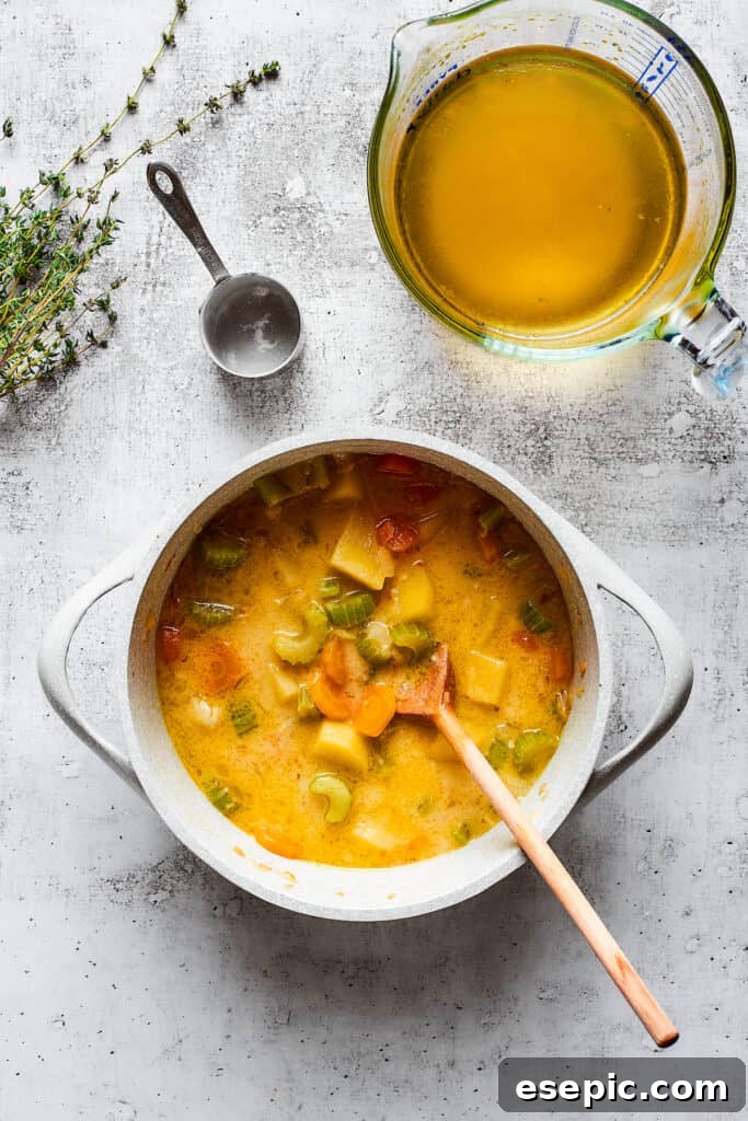 Soup simmering to thicken with broth and roux. A wooden spoon stirring a rich, thick vegetable soup in a large pot, with a measuring cup of chicken broth in the background, illustrating the thickening process.