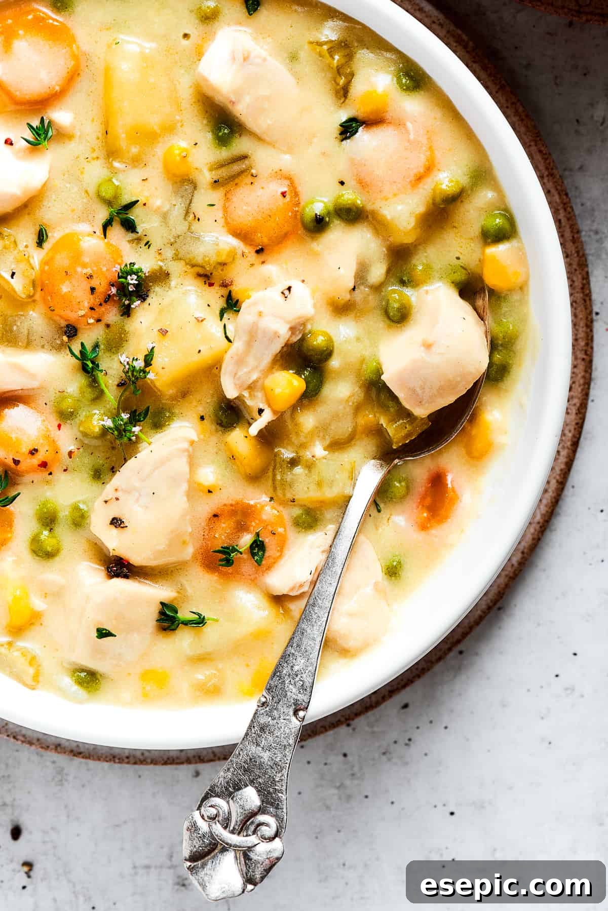 Creamy chicken pot pie soup, loaded with flavor and comfort. A close-up, inviting shot of a bowl of creamy chicken pot pie soup, rich with tender chicken and colorful vegetables, garnished with fresh thyme, with a spoon resting in the bowl.