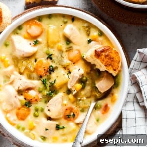 Overhead view of a bowl of chicken pot pie soup garnished with thyme, next to some biscuits.