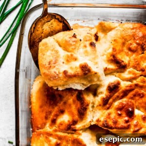 A serving spoon removing a corner piece from a pan of biscuits, showing their golden crust.