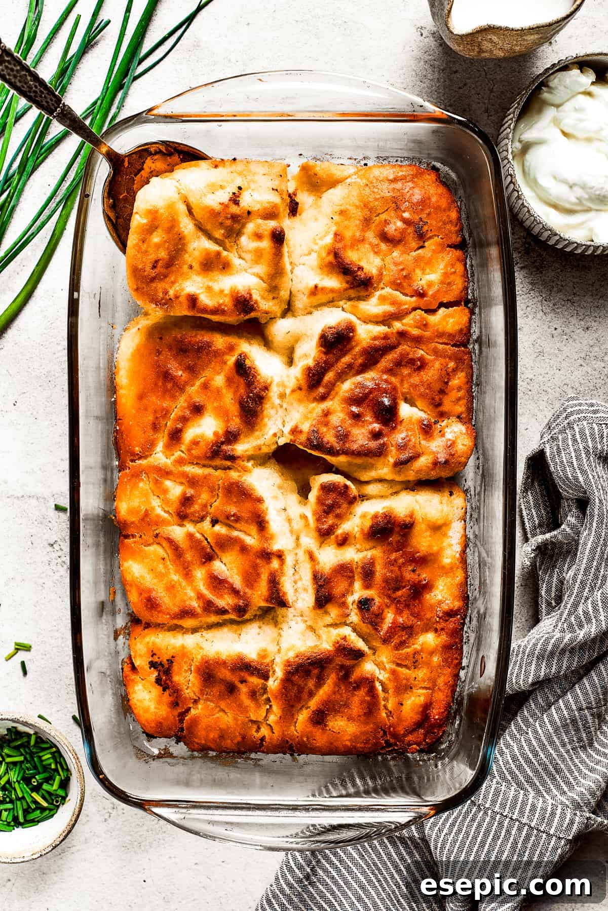 Overhead view of a baking dish full of butter swim biscuits, with a serving spoon removing a corner piece, highlighting their golden tops.