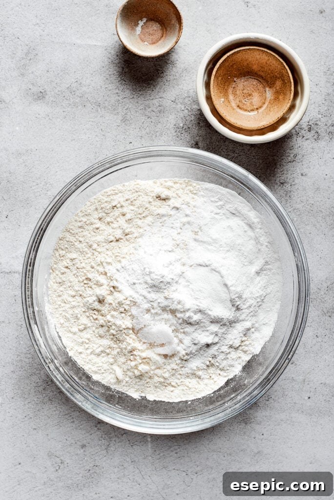 A mixing bowl full of a flour mixture, next to some small and empty bowls, ready for the next step.