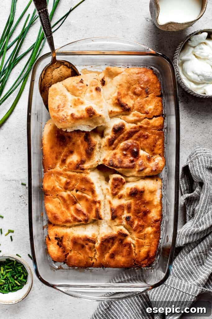 Overhead view of a baking dish full of golden-brown butter swim biscuits, with a serving spoon removing a corner piece.