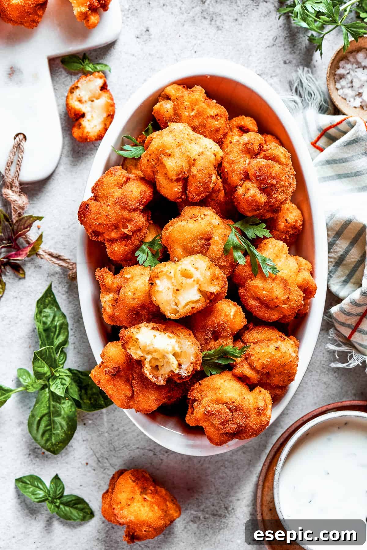 Overhead view of a serving bowl full of mac and cheese bites, next to more of them and garnished with fresh herbs.
