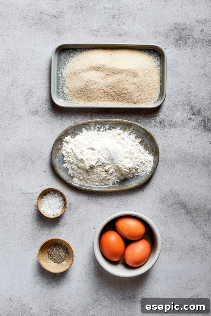 Overhead view of the ingredients needed for breading mac and cheese bites: a plate of flour, a plate of breadcrumbs, a bowl of salt, a bowl of Italian seasoning, and 3 eggs.