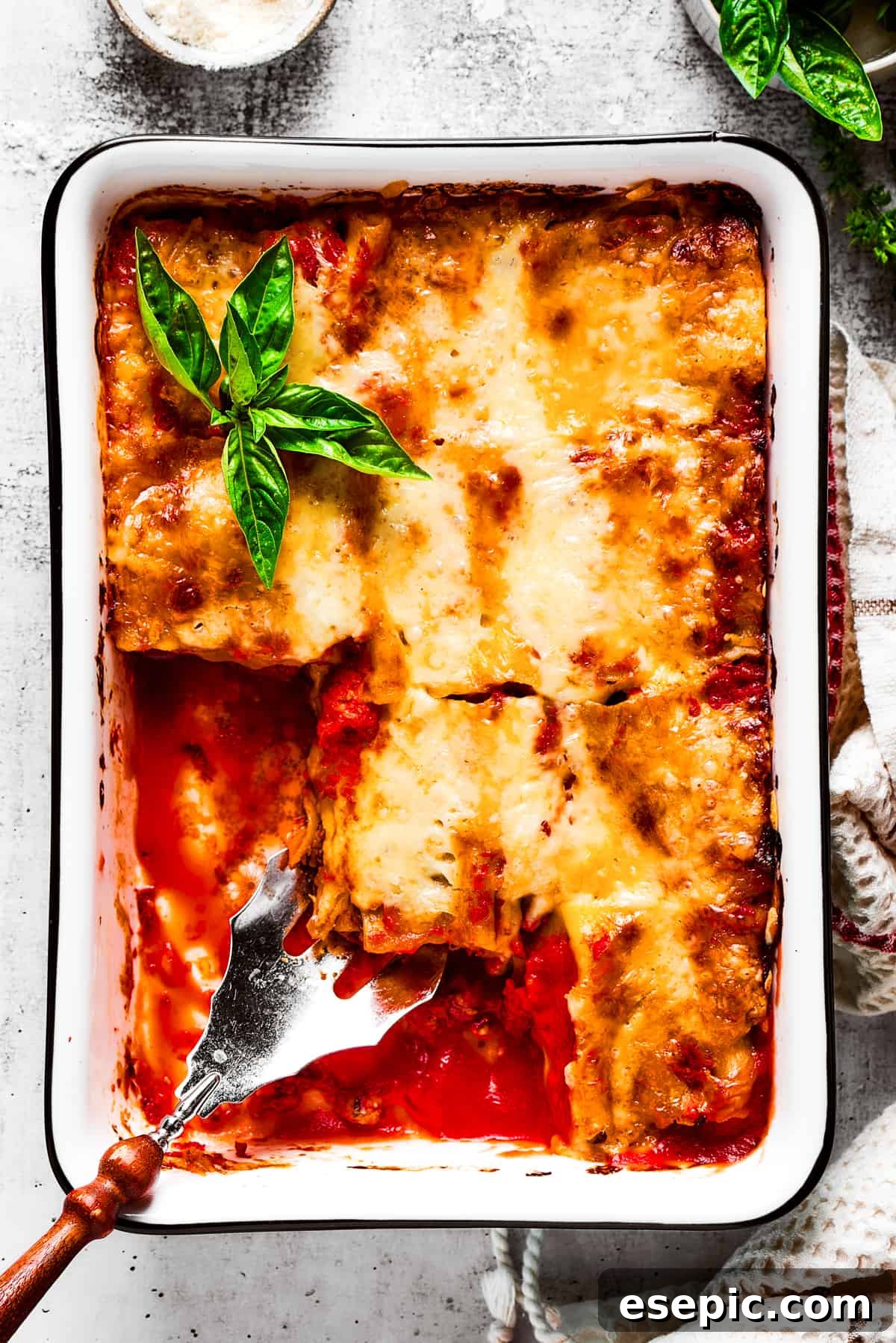 Overhead view of a baking dish filled with lasagna roll ups with a few removed, and a serving spoon removing a roll.