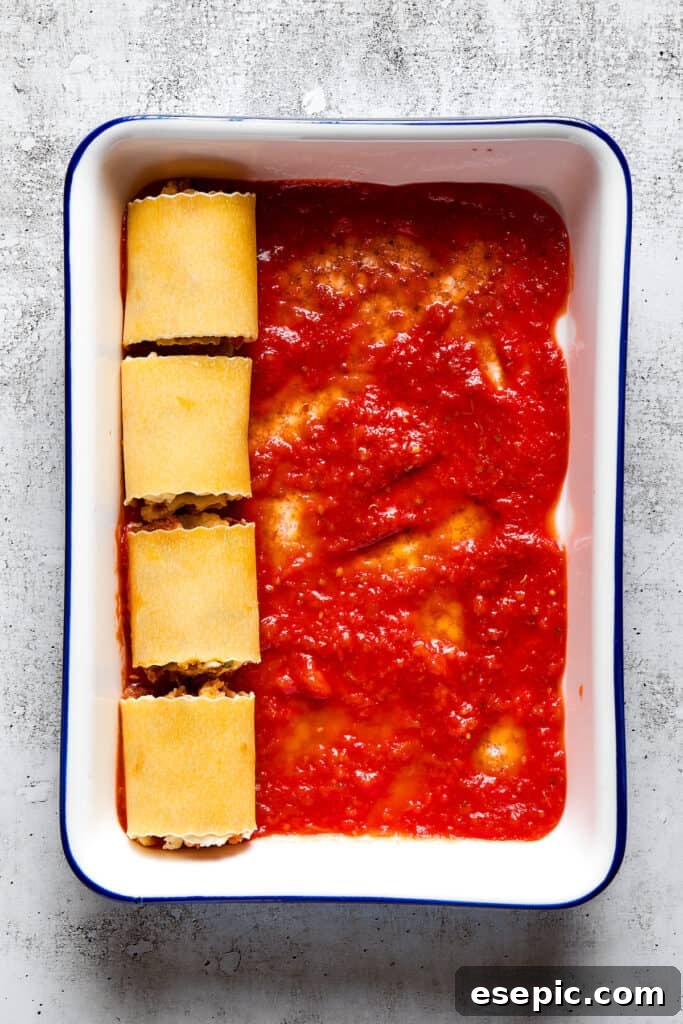 Overhead view of a baking dish partially filled with unbaked lasagna roll ups on top of marinara sauce.