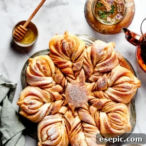 Overhead view of a star bread topped with powdered sugar, next to a bowl of honey.