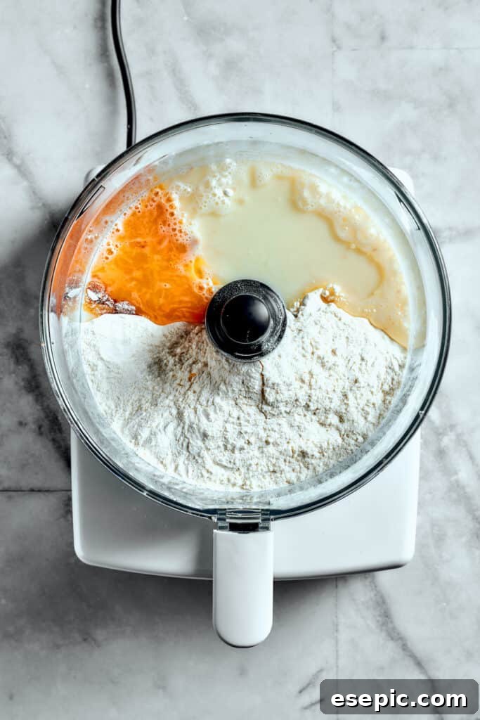 Overhead view of flour, egg yolk, milk, and yeast in a food processor.