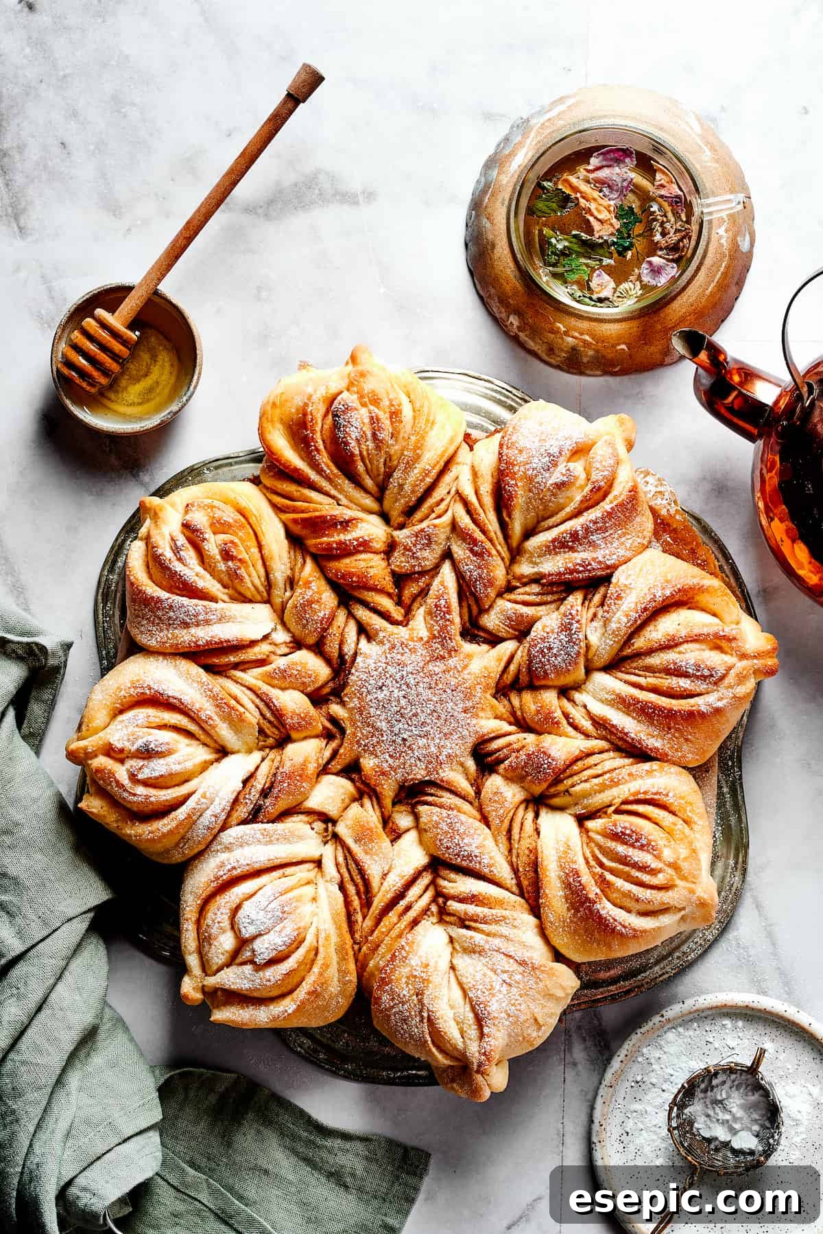 Overhead view of a star bread topped with powdered sugar, next to a bowl of honey.