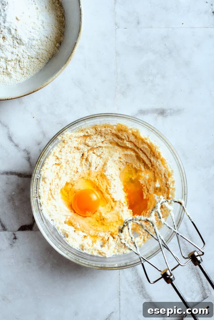 Overhead view of a mixing bowl with creamed butter and two eggs on top, with beaters.