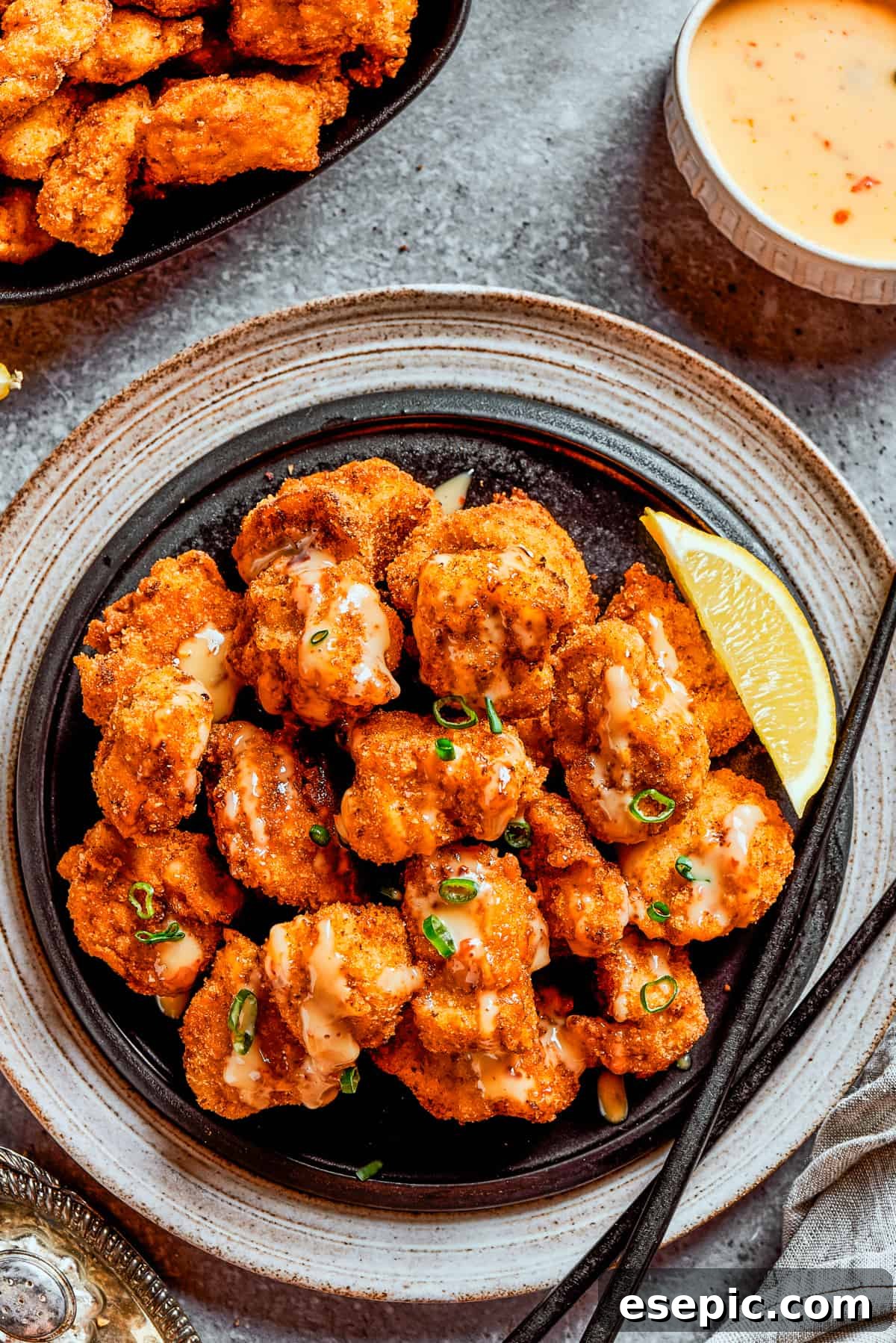 Overhead image of crispy fried bang bang chicken served on a dark dinner plate.