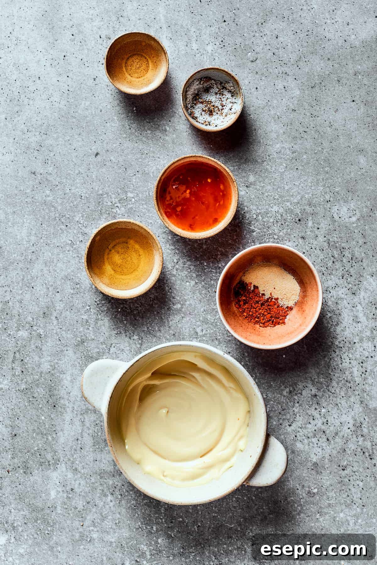 Overhead view of the ingredients needed for bang bang sauce: a bowl of mayonnaise, a bowl of sweet chili sauce, a bowl of honey, a bowl of rice vinegar, a bowl of salt and pepper, and a bowl of garlic powder and chili flakes.