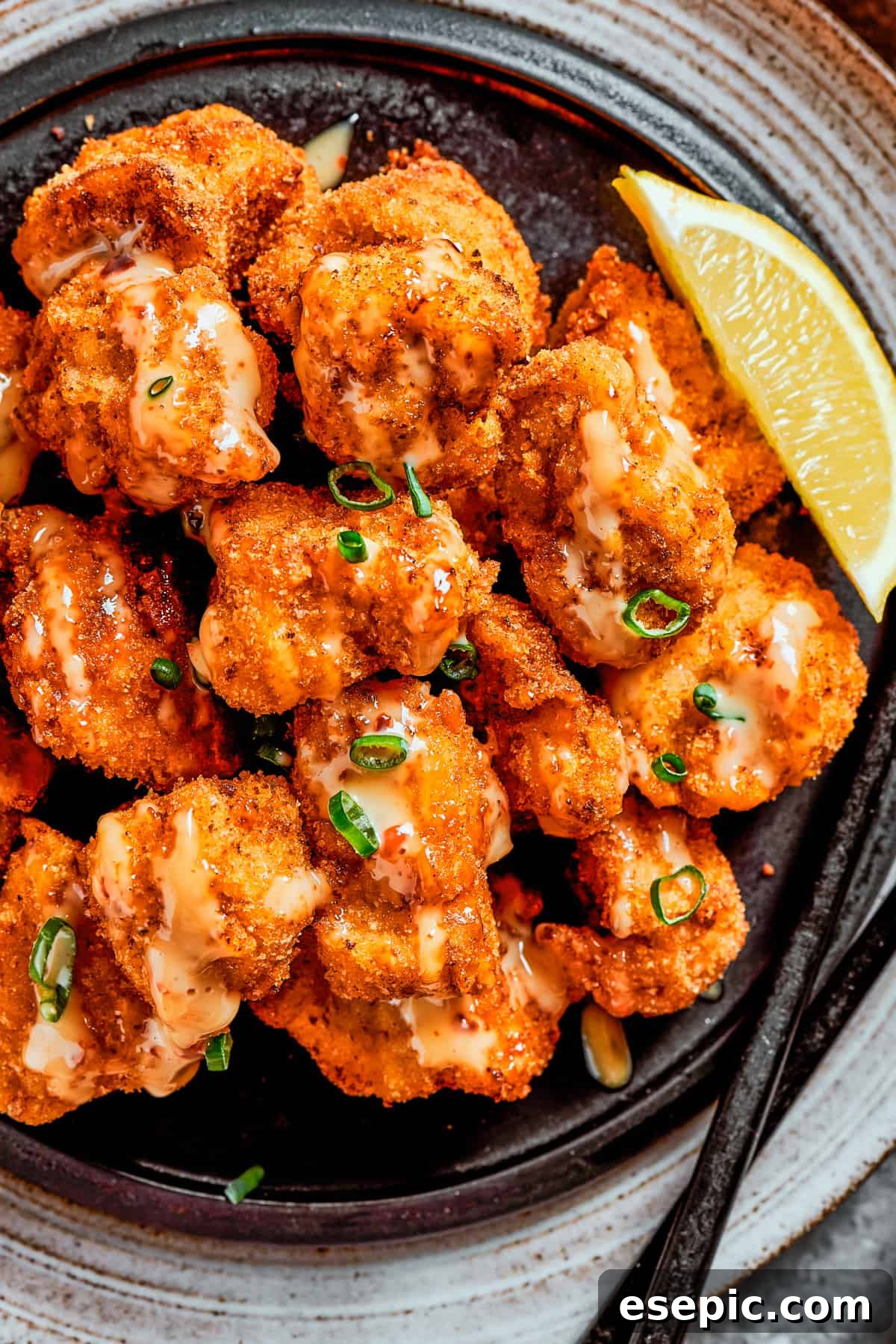 Overhead, close-up image of fried, crispy chicken bites topped with sauce and served with a lemon slice.