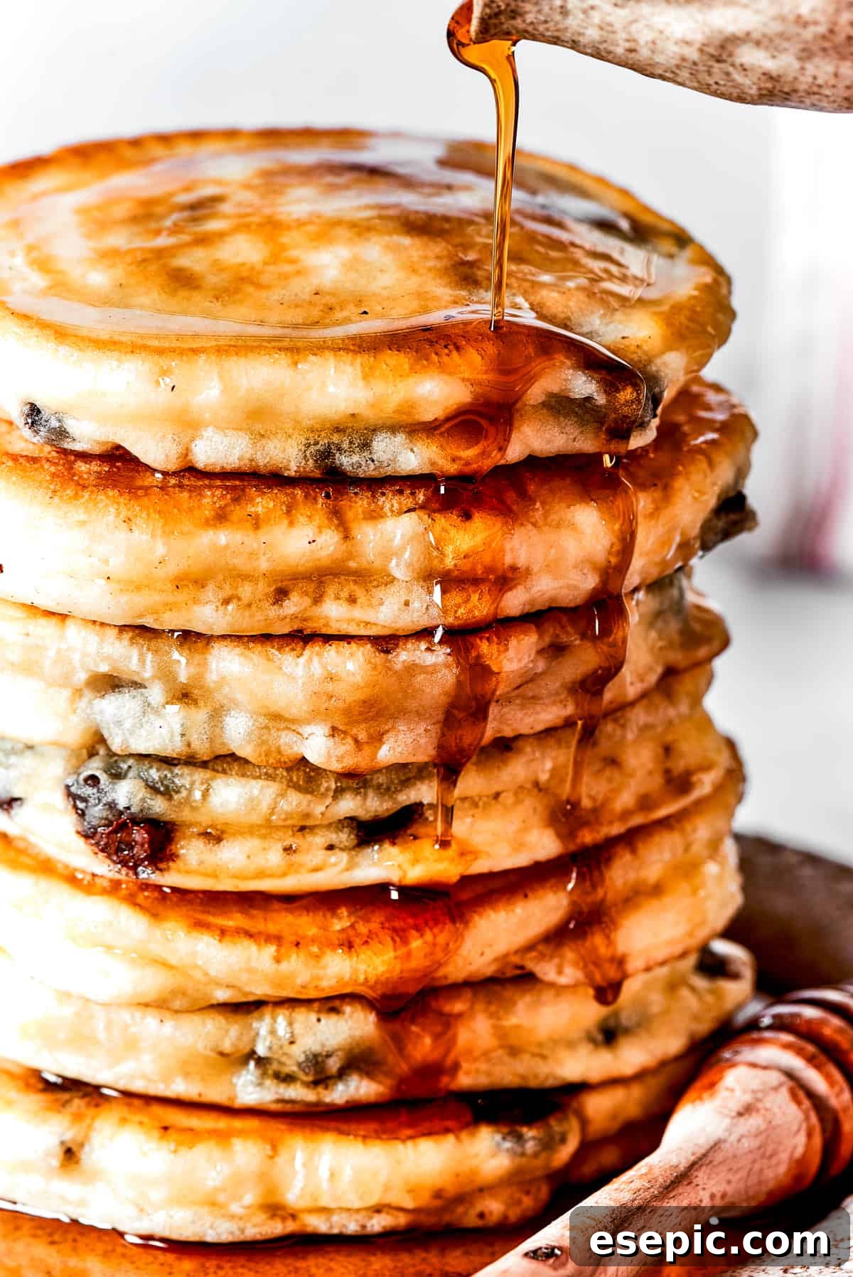 Pouring maple syrup over a stack of fluffy pancakes.