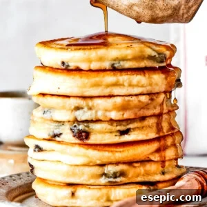 Pouring maple syrup over a stack of chocolate chip pancakes.