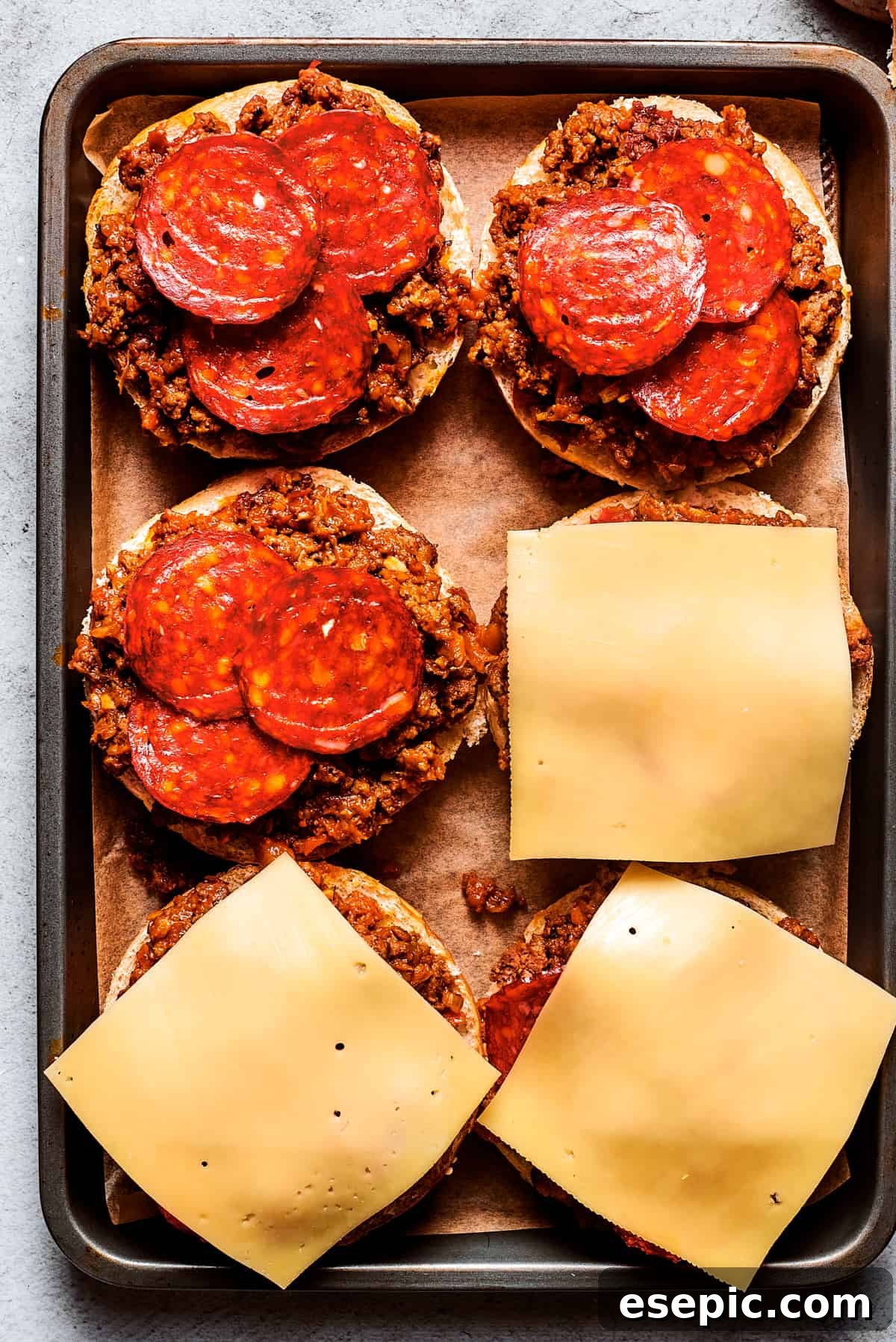 Melted mozzarella cheese and pepperoni generously top savory pizza burgers on a baking sheet, ready to be served.