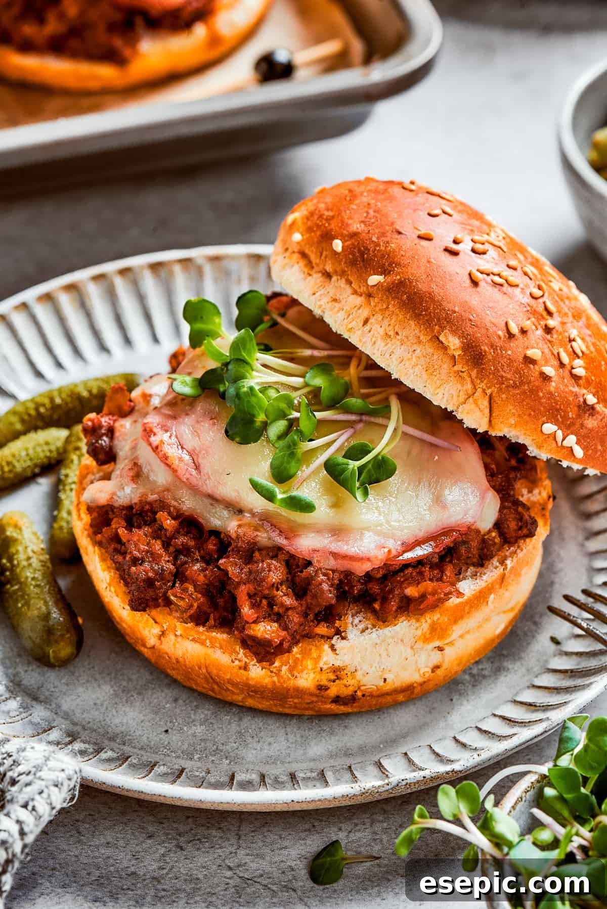 A freshly broiled pizza burger, with its top bun playfully resting aside, reveals a generous filling of seasoned meat, melted mozzarella, and savory pepperoni.