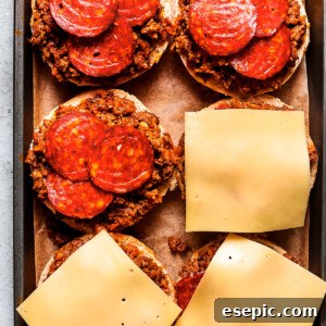 Cheese slices are placed on top of pizza burgers on a tray.
