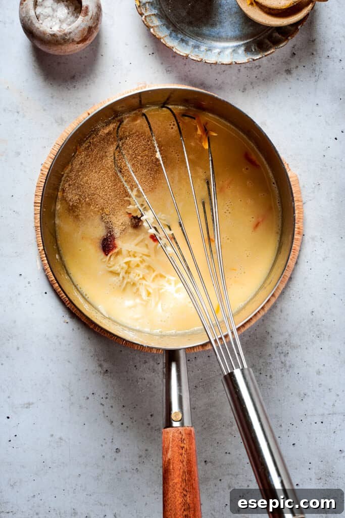 Master the art of homemade soft pretzels and pair them with our decadent, mustard-infused cheese dip. A metal whisk continues to blend a rich, bubbling cheese sauce in a metal pot, highlighting its creamy texture and inviting readiness.