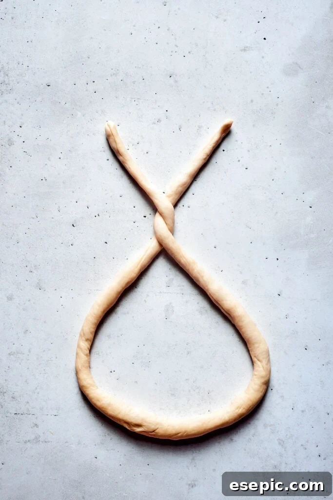 Master the art of homemade soft pretzels and pair them with our decadent, mustard-infused cheese dip. A skilled hand demonstrates the initial twist of a soft pretzel dough rope, forming the iconic top loops before sealing the ends.