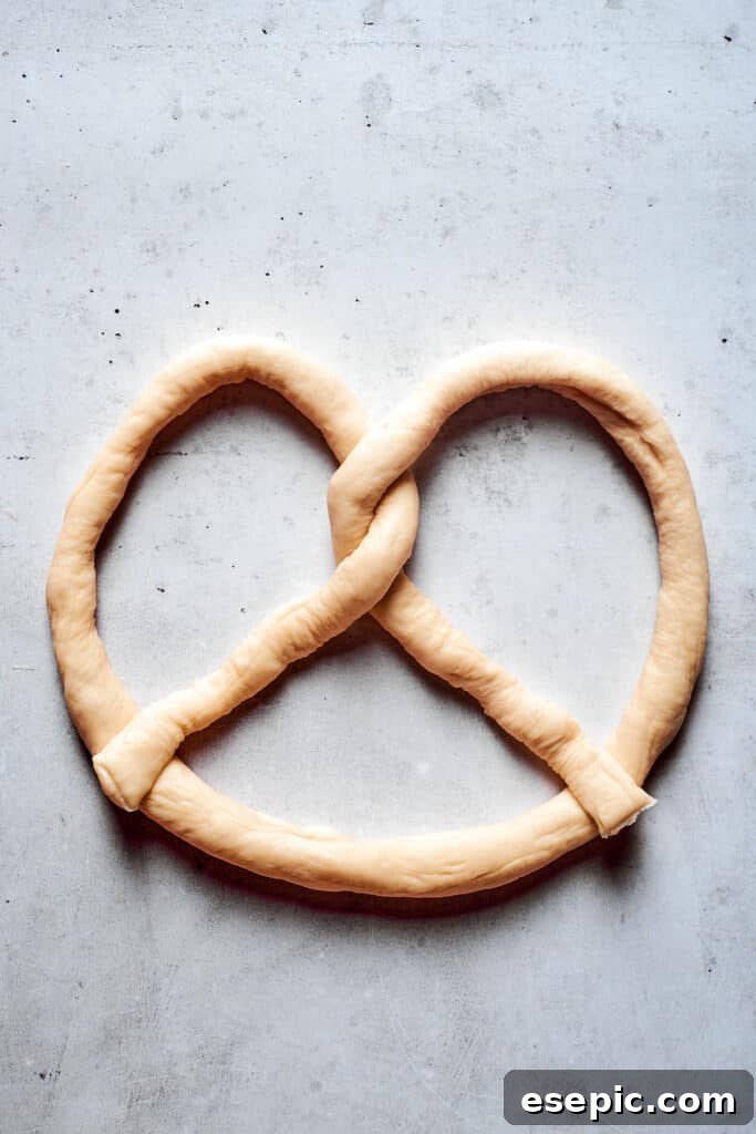 Master the art of homemade soft pretzels and pair them with our decadent, mustard-infused cheese dip. The final step in pretzel shaping, as the twisted ends of the dough rope are pressed firmly into the base of the 'U' to create the classic shape.