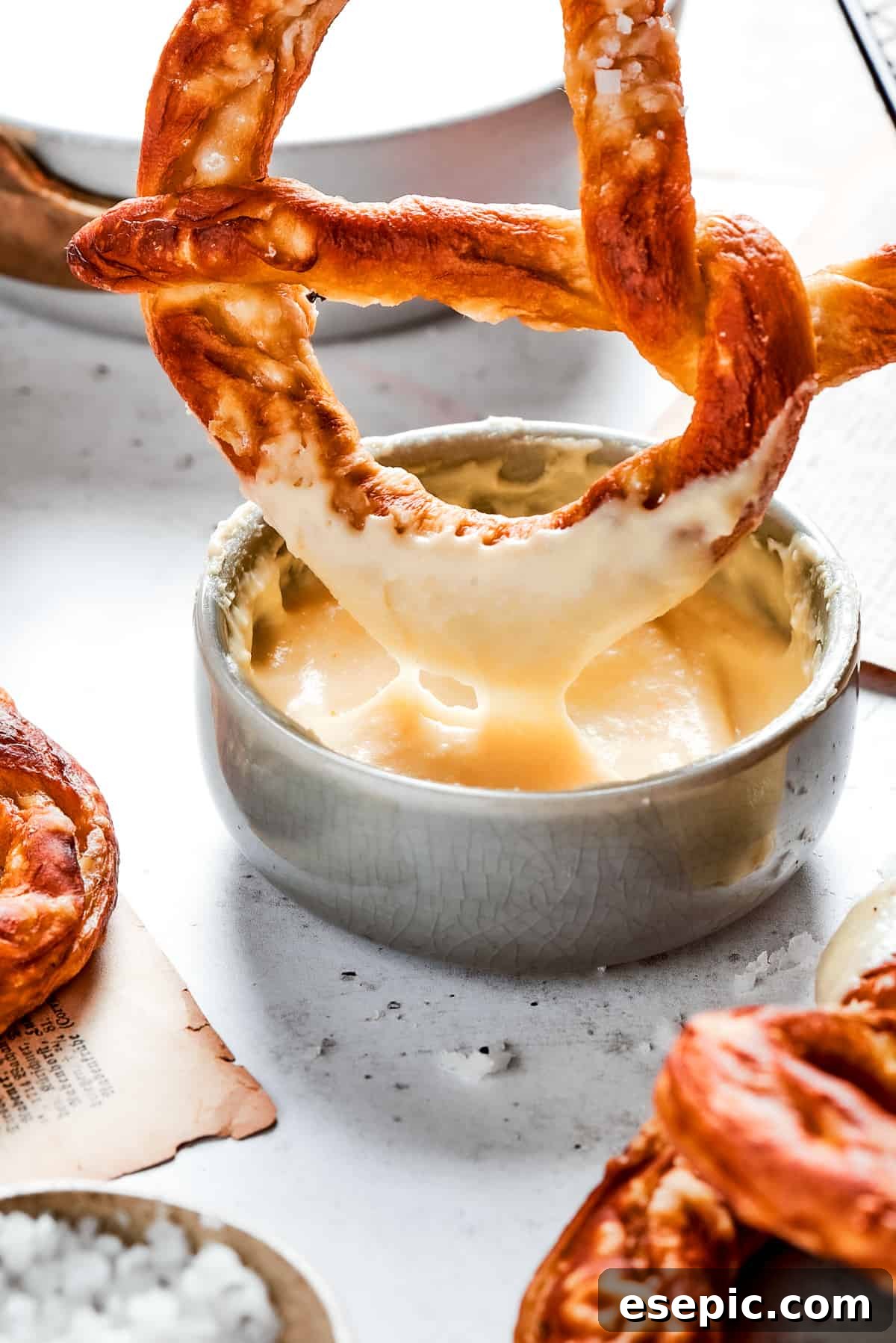 Master the art of homemade soft pretzels and pair them with our decadent, mustard-infused cheese dip. A perfectly baked, golden soft pretzel is being dipped into a luscious, creamy cheese sauce, creating an irresistible moment.