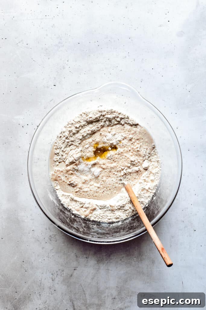Master the art of homemade soft pretzels and pair them with our decadent, mustard-infused cheese dip. A glass bowl holds a perfectly risen, soft pretzel dough, a wooden spoon resting nearby, indicating readiness for the next stage.