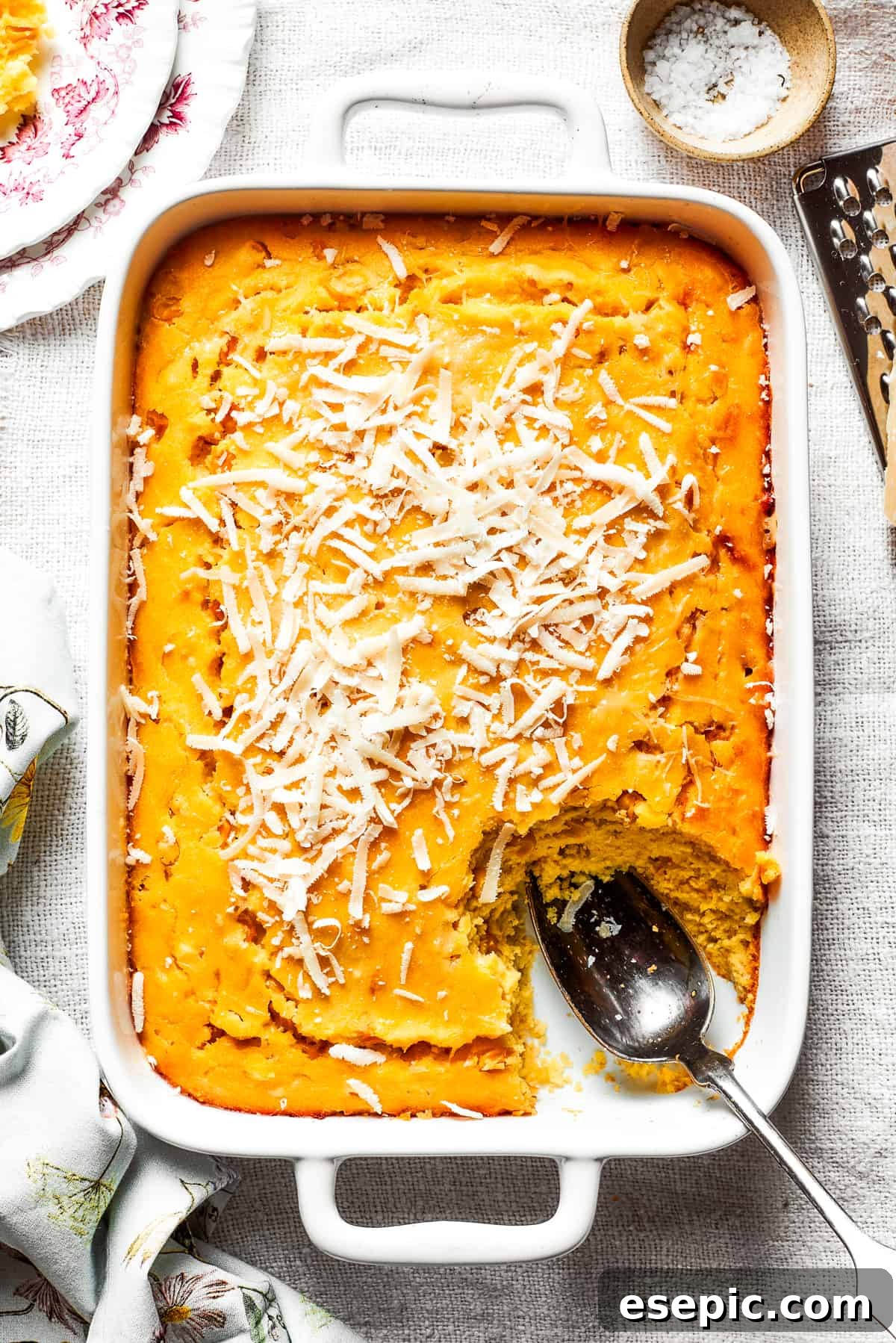 A white baking pan of baked corn souffle with a piece cut out and a spoon in the lower right side, showcasing its rich, creamy texture.