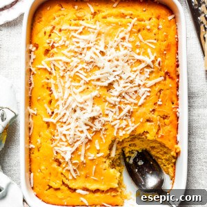 A white baking pan of baked corn souffle with a piece cut out and a spoon in the lower right side, ready to serve.