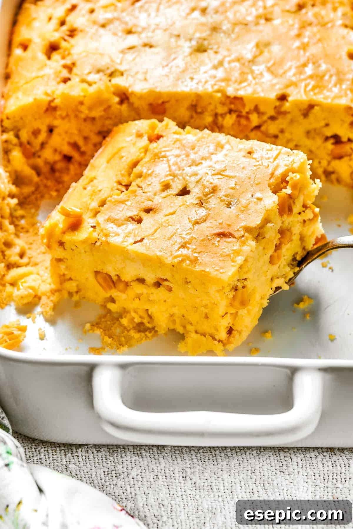 A perfectly cut-out square of golden brown corn souffle inside a white baking dish, ready to be served.