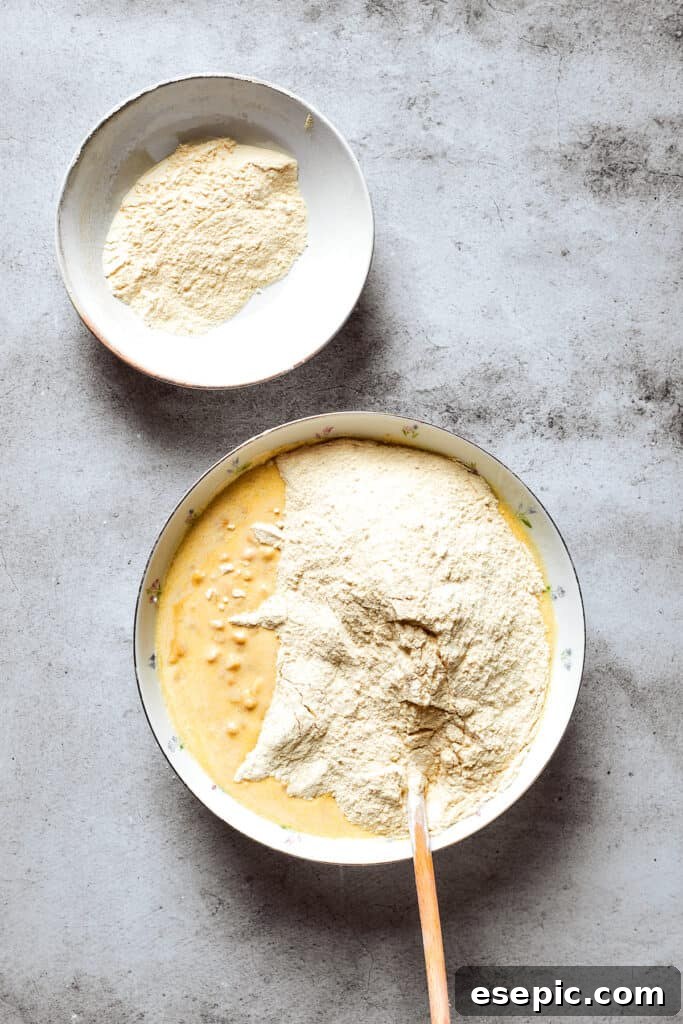 Cornbread mix is being added to a bowl of corn souffle base ingredients, ready to be stirred.