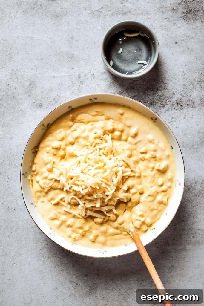 Shredded cheddar cheese is being added to a bowl of corn souffle batter, ready for its savory addition.